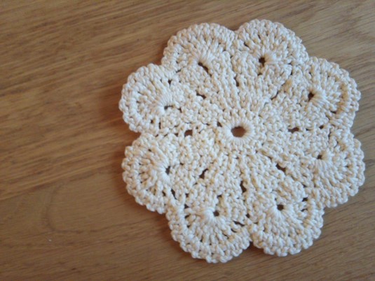 A white crochet doily on a wood surface Description automatically generated